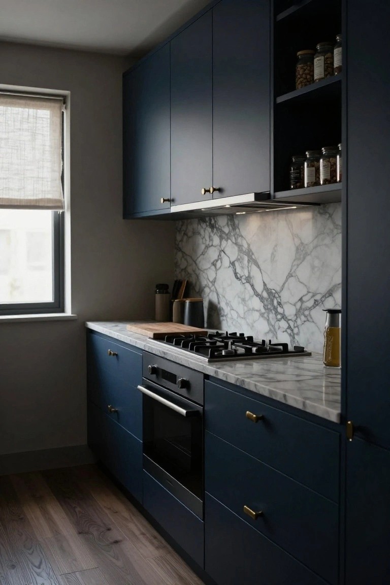 Kitchen with navy blue cabinets, white marble backsplash and countertop featuring dramatic gray veining, gas cooktop, oven, gold handles, wooden cutting boards, jars on open shelves, and hardwood flooring next to a window.