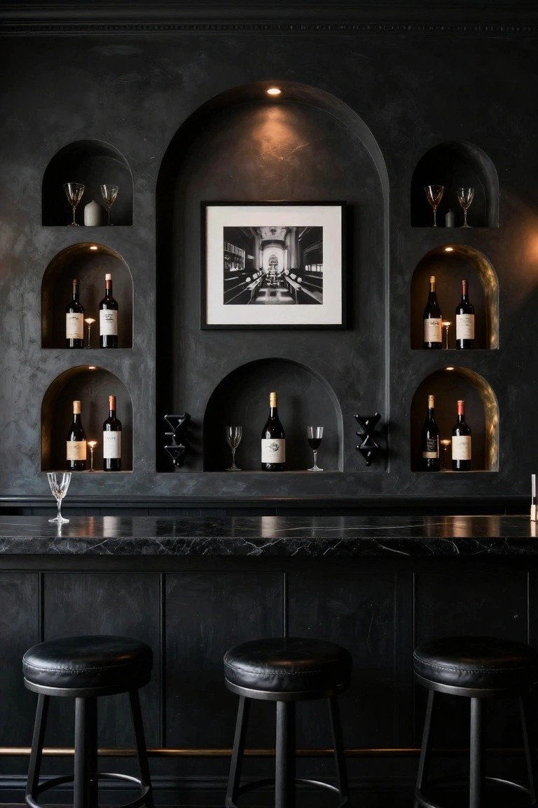 Dark textured wall with multiple arched niches displaying wine bottles, glassware, candles, and a central black-and-white framed photo of an interior, above a black marble bar counter with three black leather stools.