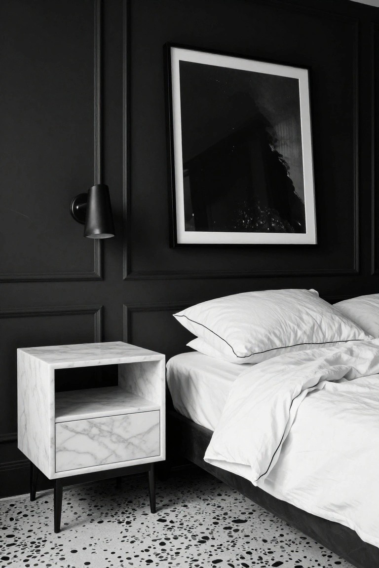 Bedroom corner with black paneled walls, white marble cube nightstand on black legs beside a white bed with pillows and duvet, black wall sconce, and large framed abstract black-and-white photo.
