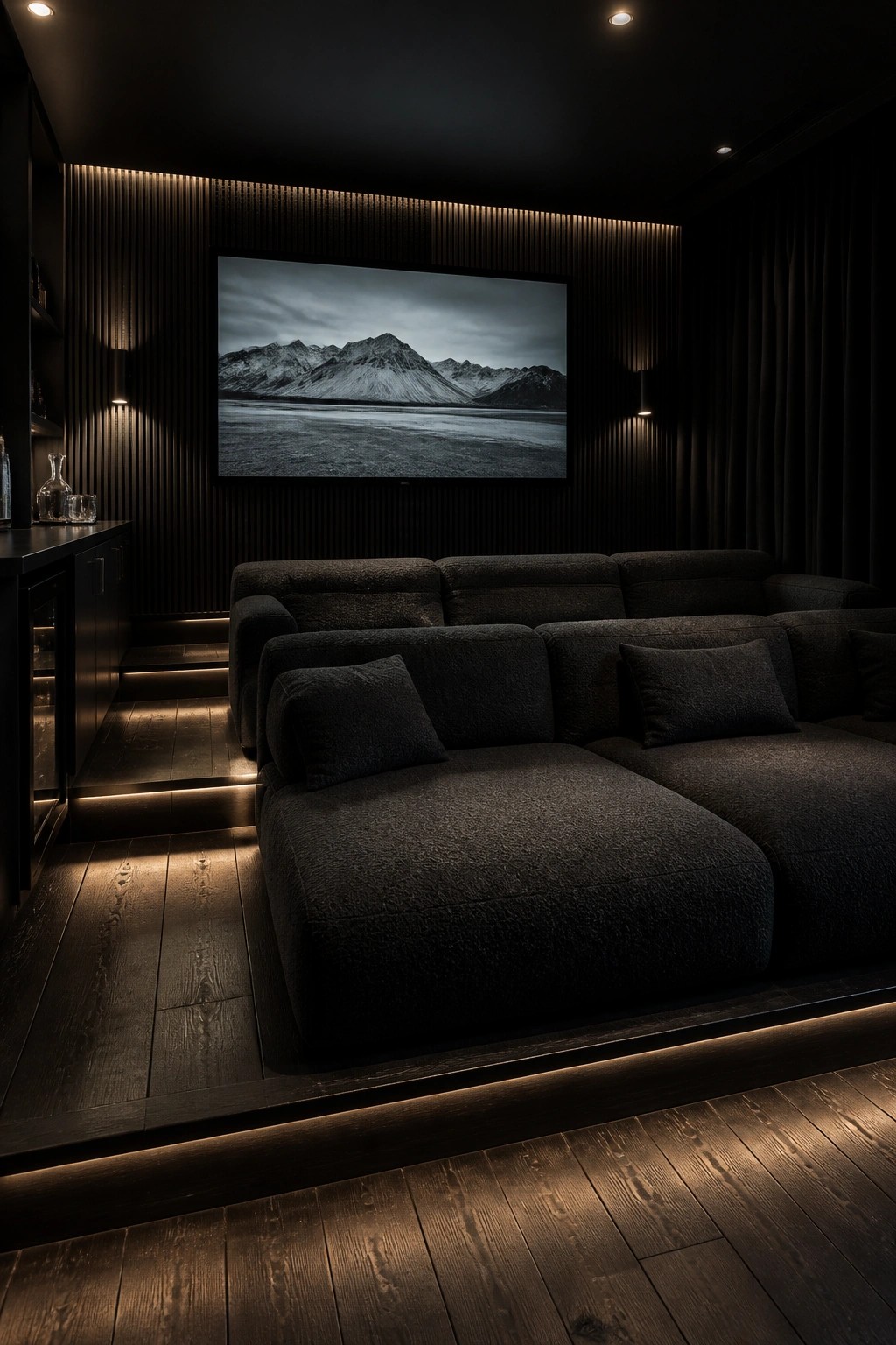 A dark home theater with a large sectional sofa facing a wall-mounted TV showing a mountain landscape, with backlit wood slat panels on the wall behind the screen.