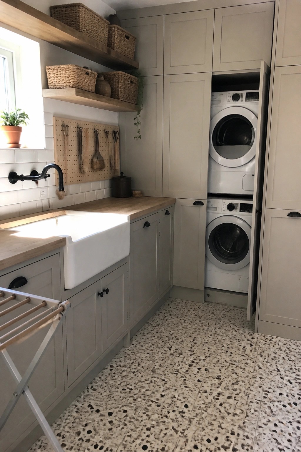 Modern laundry room with gray cabinets, white sink, stacked washer-dryer, and terrazzo floor.
