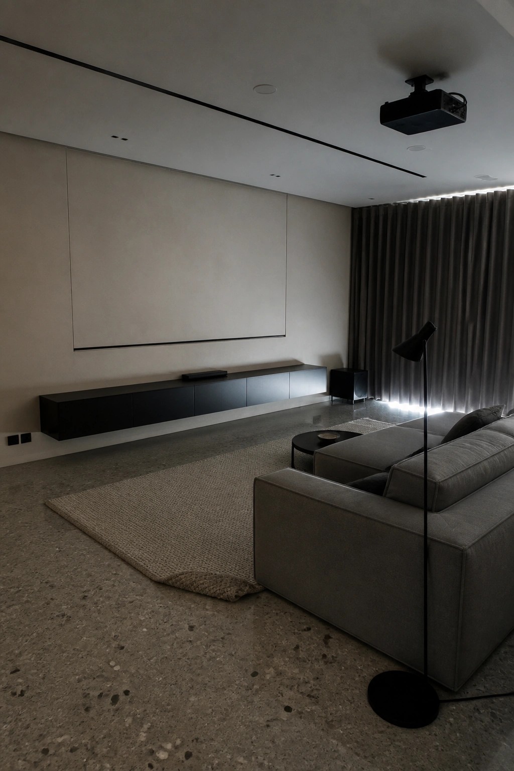 Minimalist living room with gray sofa, black media console, ceiling projector, and large screen.