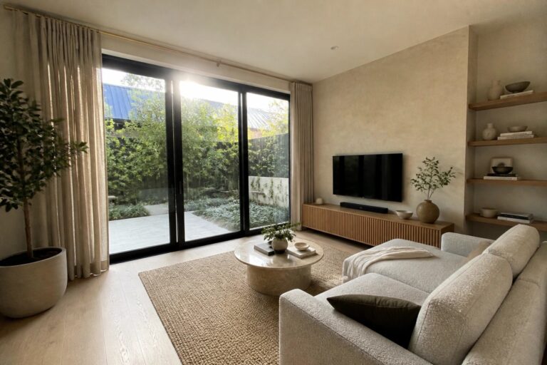 21 Space-Smart Luxury Sliding Doors With Large Glass Panels A living room with a large sliding glass door open to a patio that includes a potted tree, outdoor chair, and round water feature.