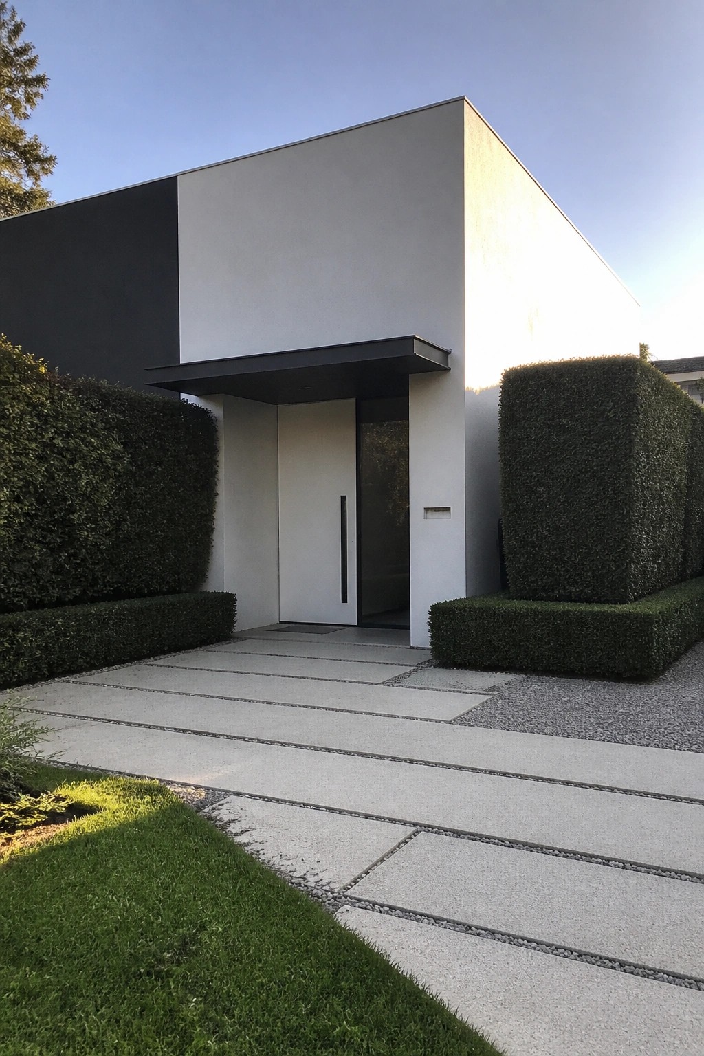 Modern minimalist house entrance with white door, concrete steps, and green hedges