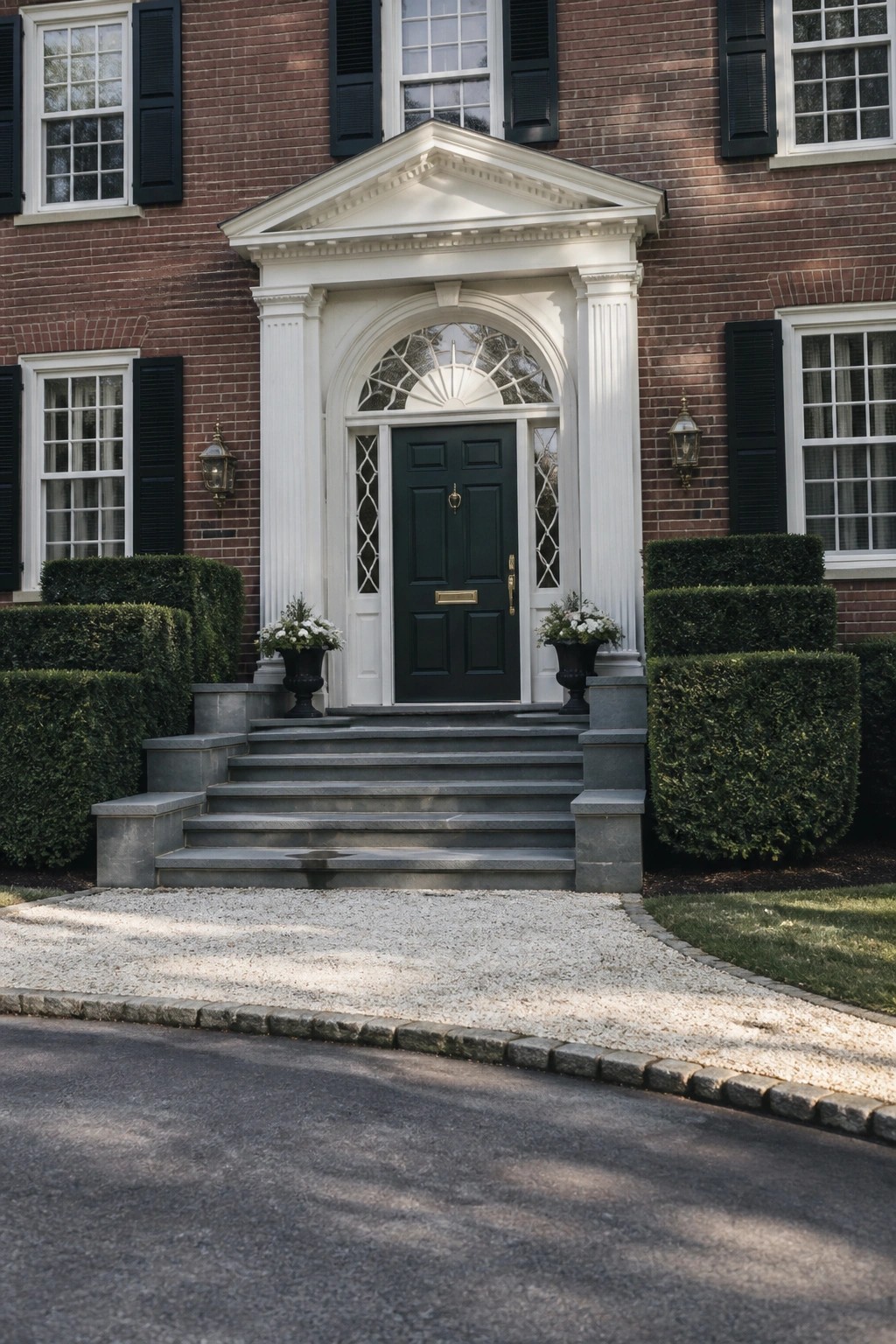 A brick house with a white columned portico and pediment framing a dark green front door above gray stone steps.