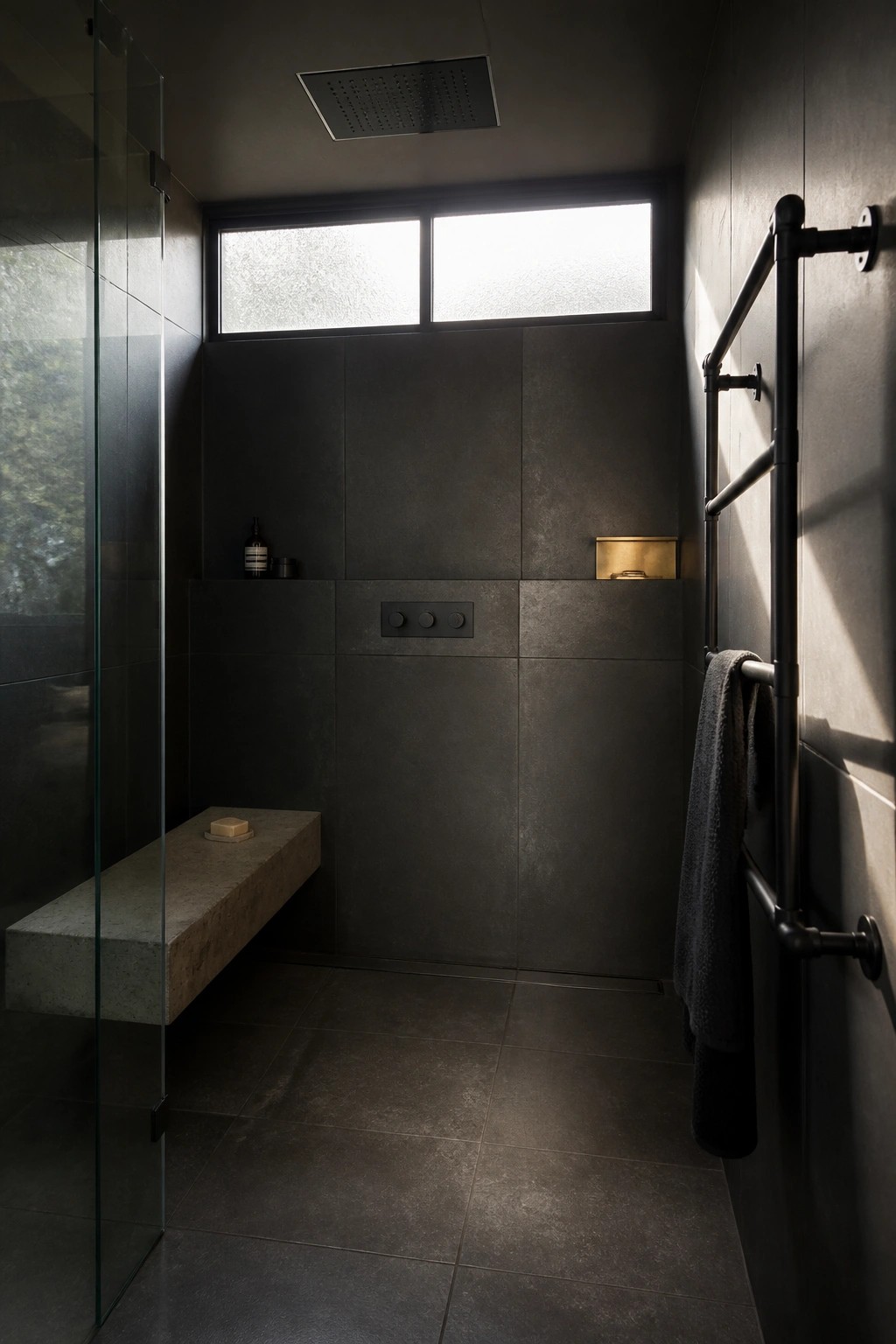 A dark tiled shower with a small flush control panel centered on the back wall and a concrete bench on the left.