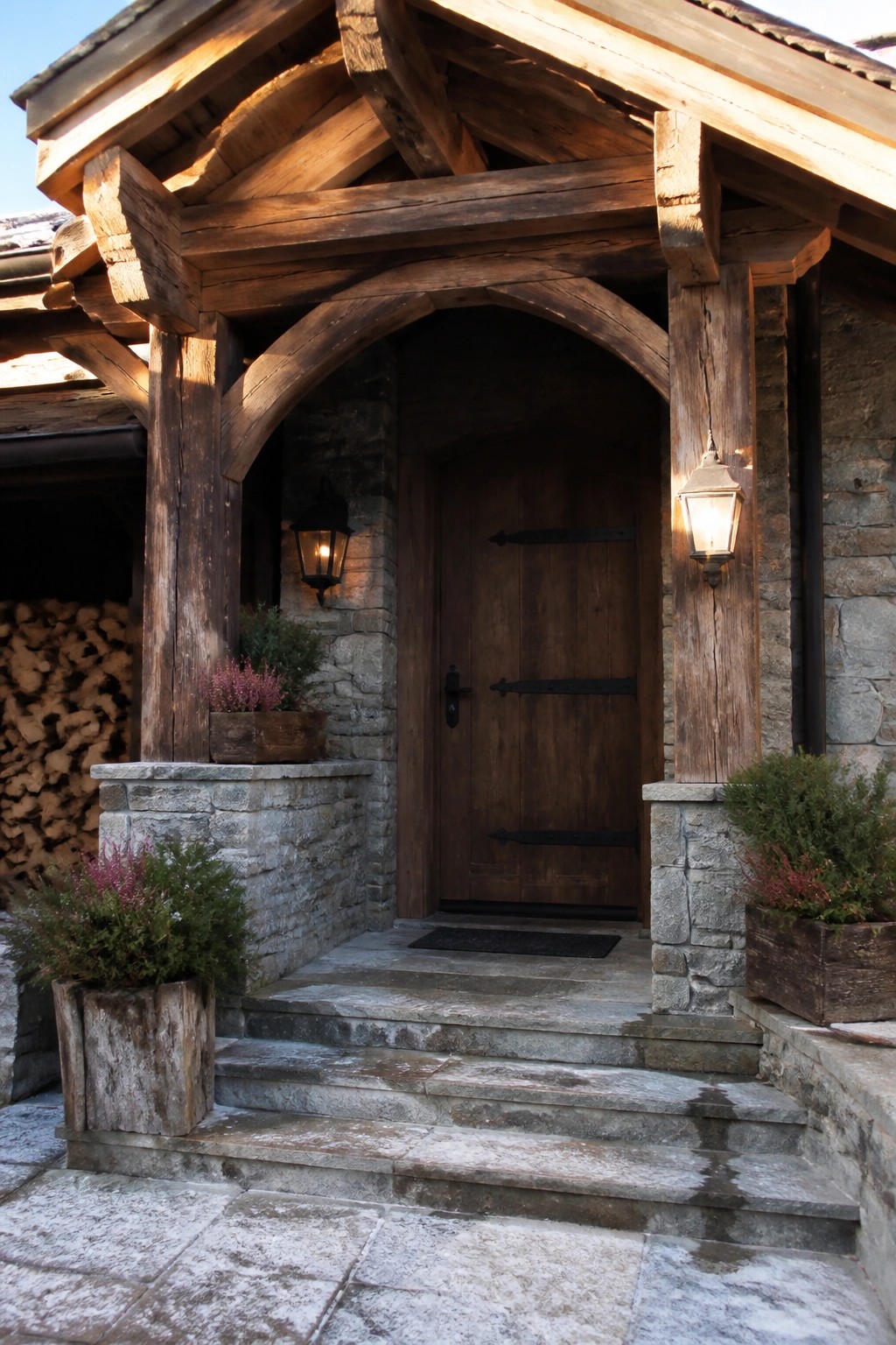 Rustic timber porch with arched wooden door, glowing lanterns, and stone steps with plants