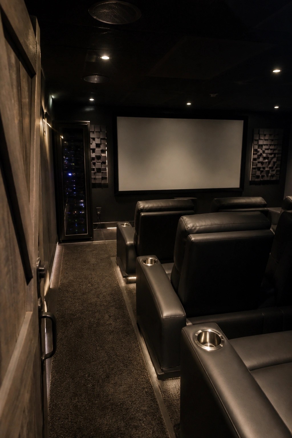 Dimly lit home theater with black leather recliners facing blank screen.