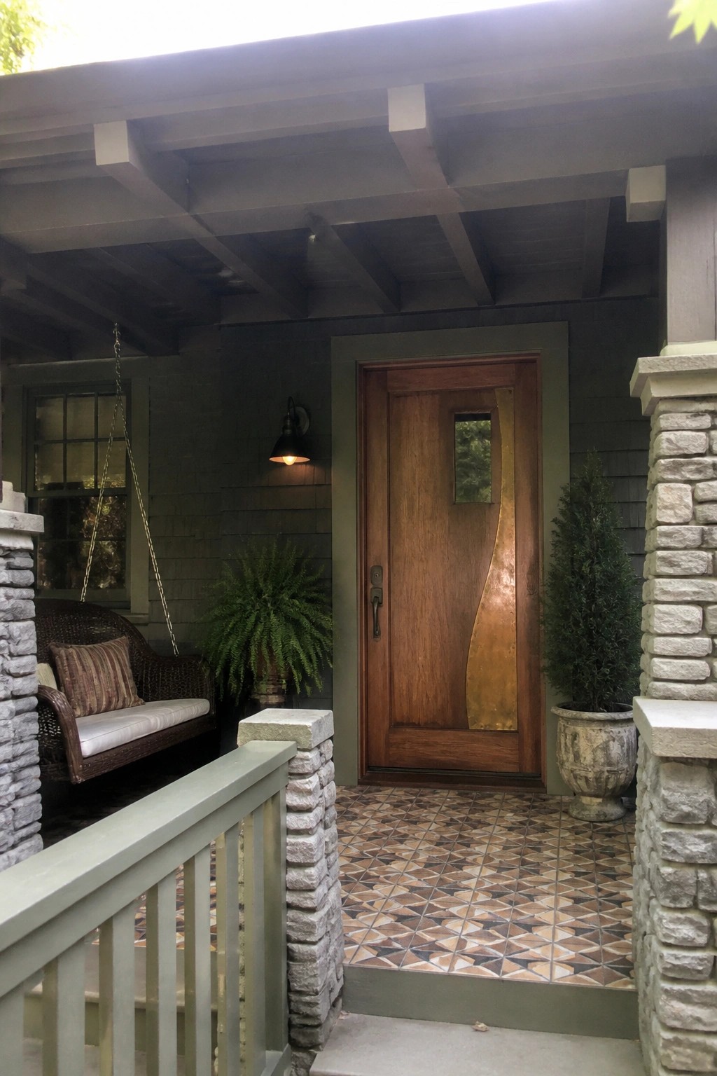 Porch with geometric tiled floor, wooden door with curved copper panel, hanging swing