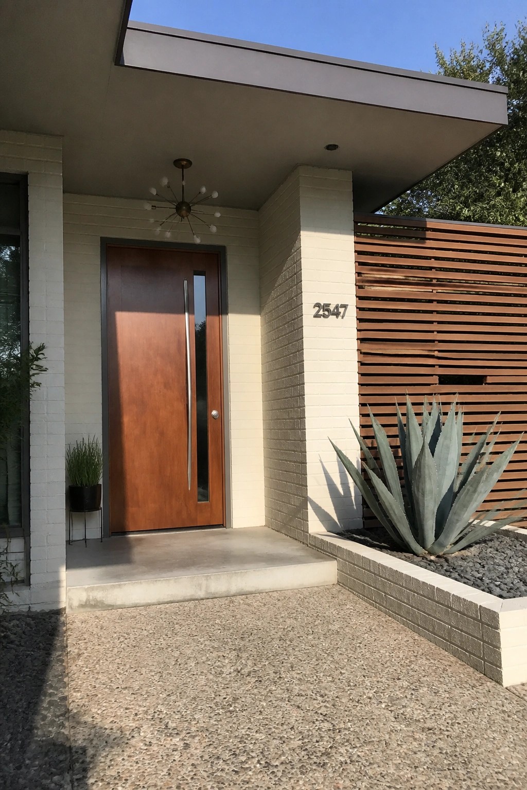 Modern home entrance with wooden door, white brick, agave plant, and house number 2547.